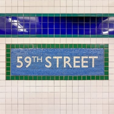 Subway wall sign displaying 59th Street in white text on a blue tile background with green borders. Blue and white tiles surround the sign.